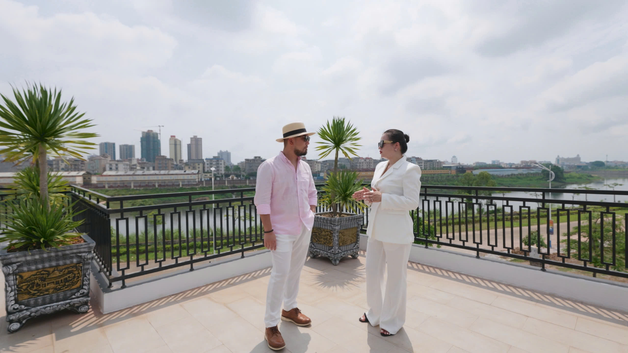 Hai người trò chuyện trên sân thượng có view thành phố và sông.