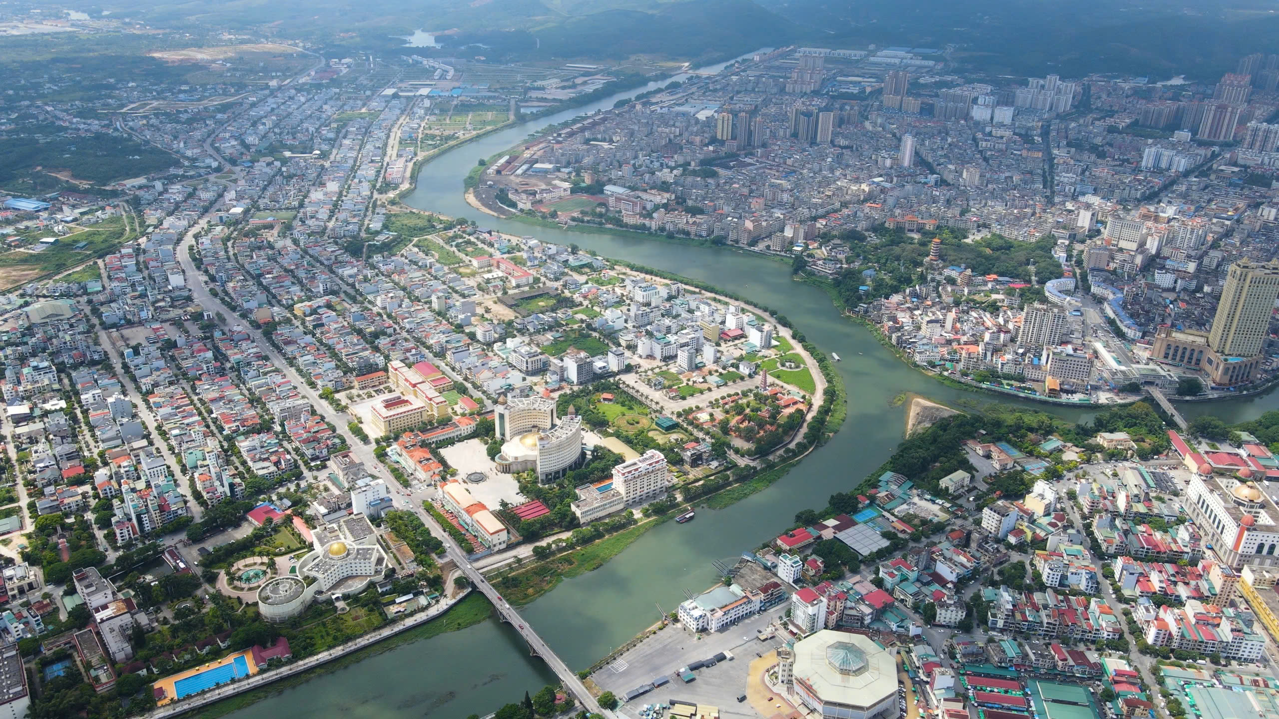 Cảnh quan thành phố với dòng sông uốn lượn, kiến trúc đa dạng và khu nhà chọc trời từ phía trên.