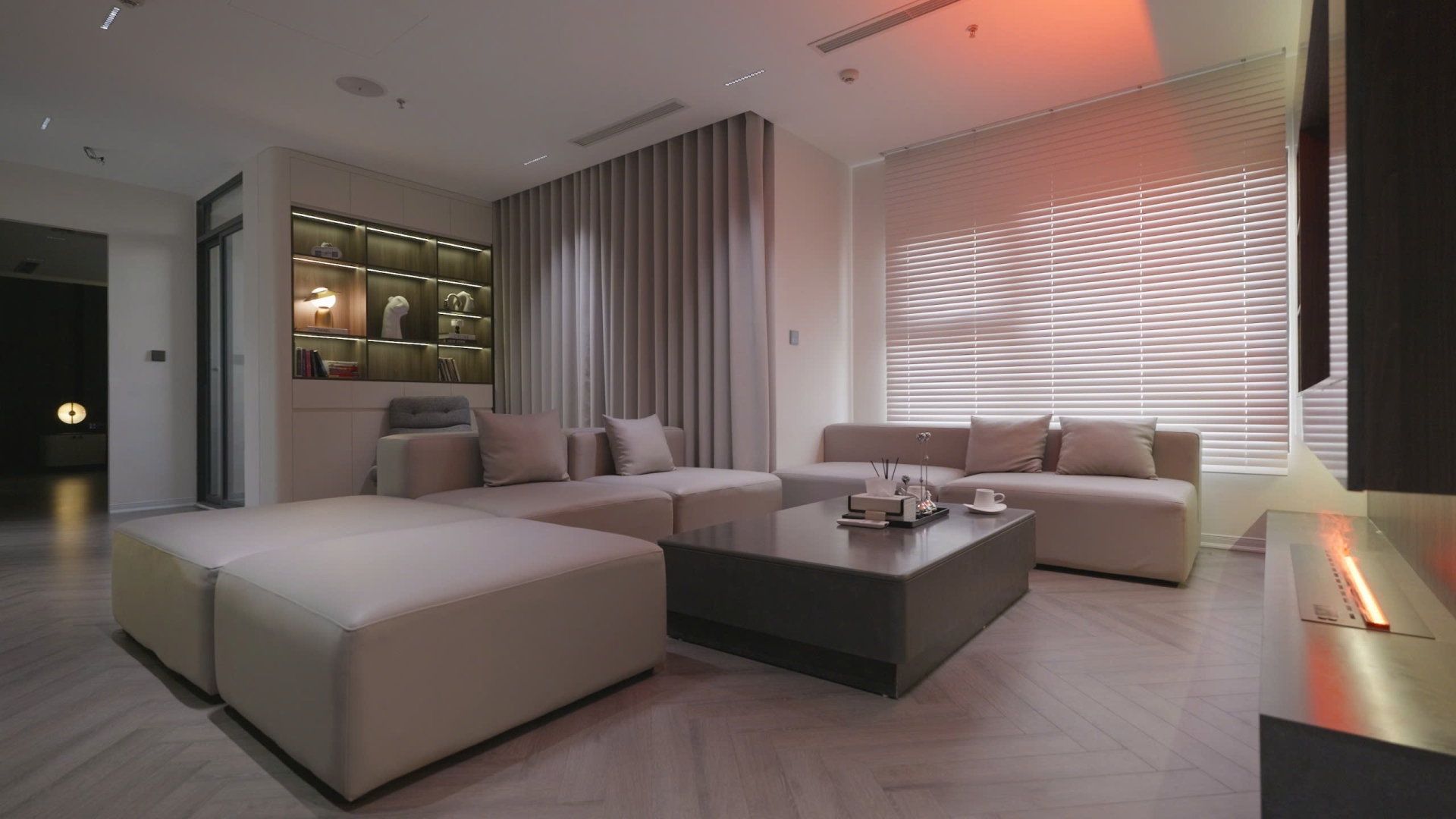 zgnujo18rmfq62dexykb Phòng khách hiện đại với sofa xám nhạt, bàn trà đen, rèm cửa sáng và trang trí gỗ sang trọng.